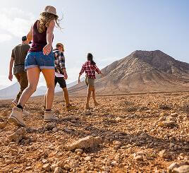 Grupo de personas caminando sobre terreno pedregoso, con paisaje volcánico al fondo.
