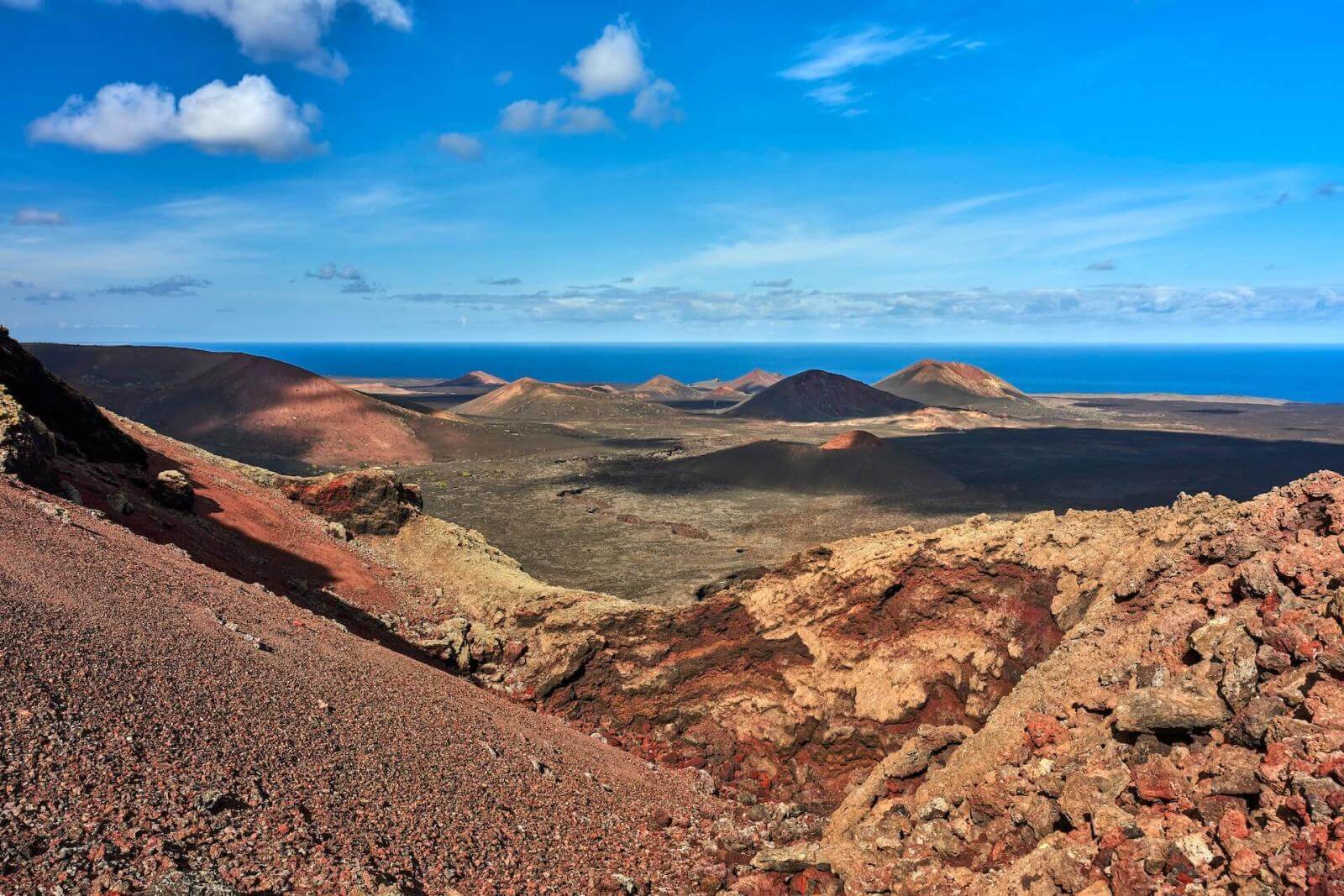 Paisaje volcánico con coladas de lava y montañas y mar de fondo en Parque Nacional de Timanfaya, Lanzarote.