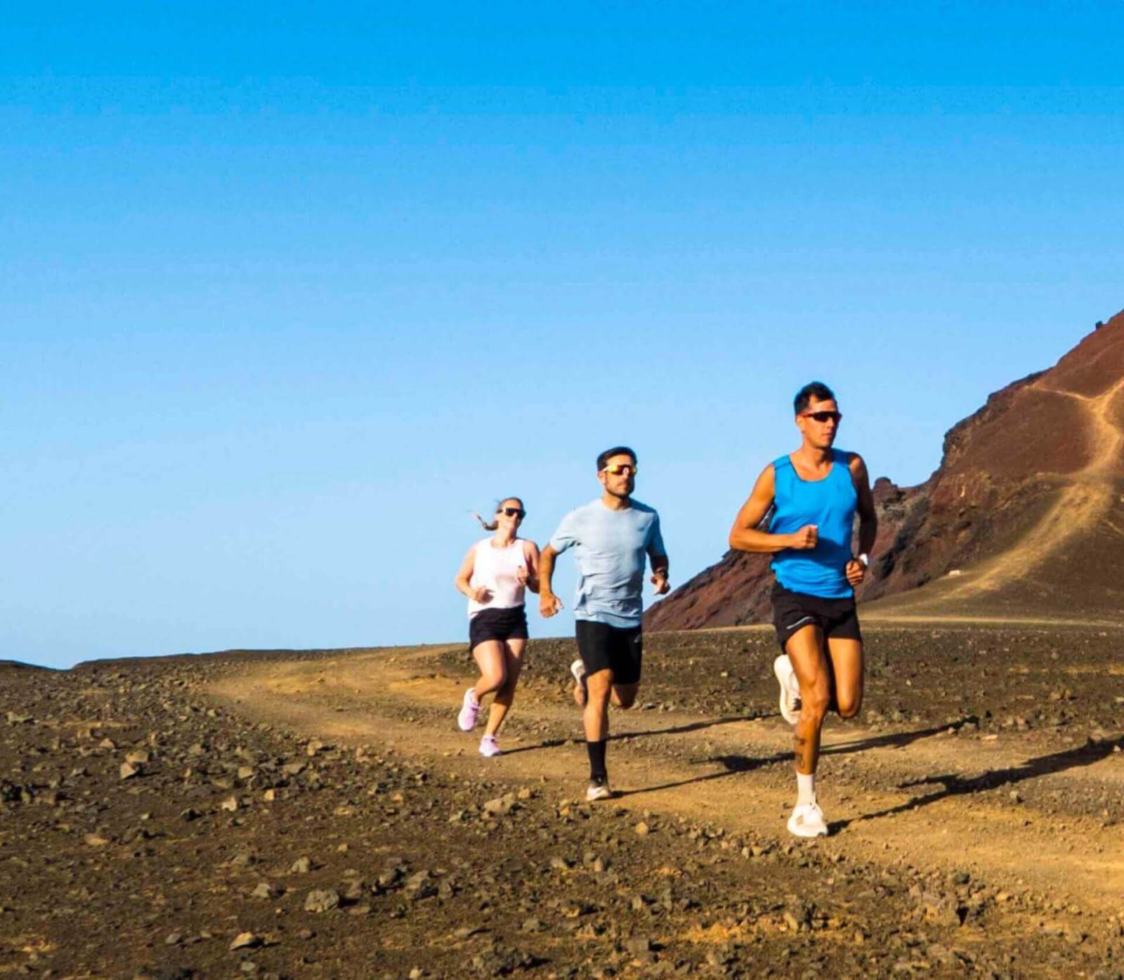 Tres atletas entrenando en sendero amplio de terreno volcánico bajo cielo despejado.