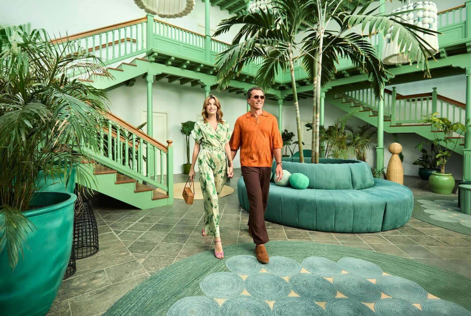 Pareja caminando por un vestíbulo inspirado en la arquitectura tradicional canaria, con luz y vegetación tropical.