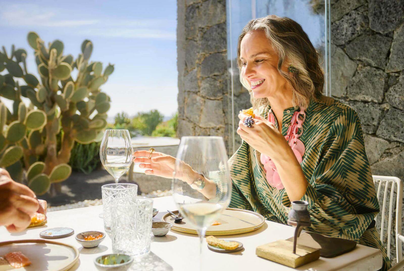 Persona disfrutando de aperitivo y copa de vino en una mesa junto a puerta de terraza con cactus al fondo.