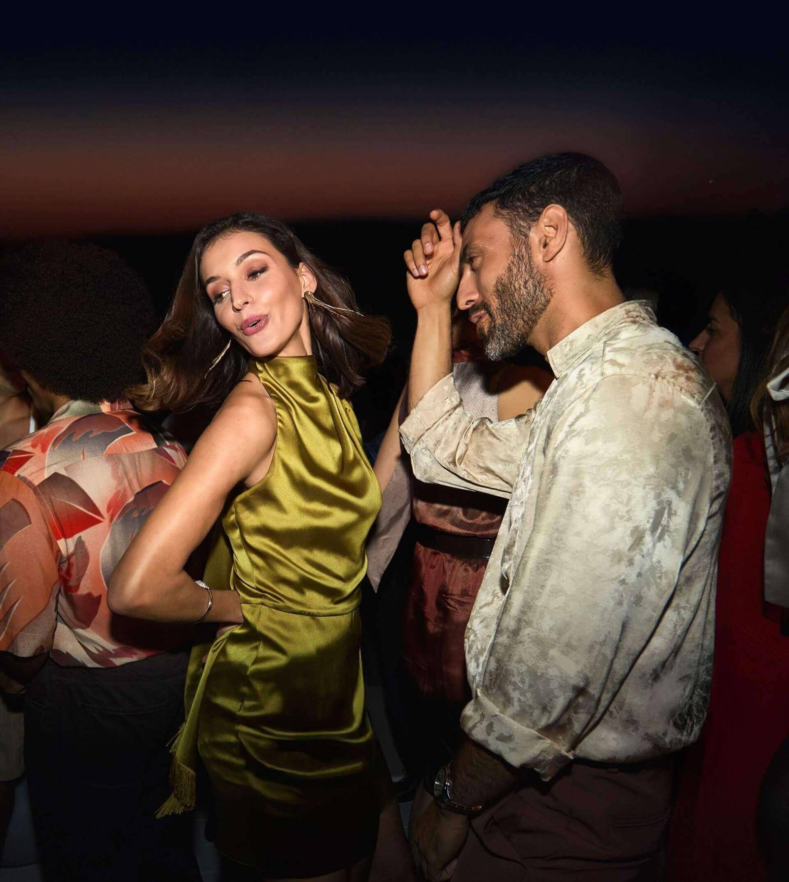 Pareja bailando en terraza rooftop con vistas al mar al anochecer.