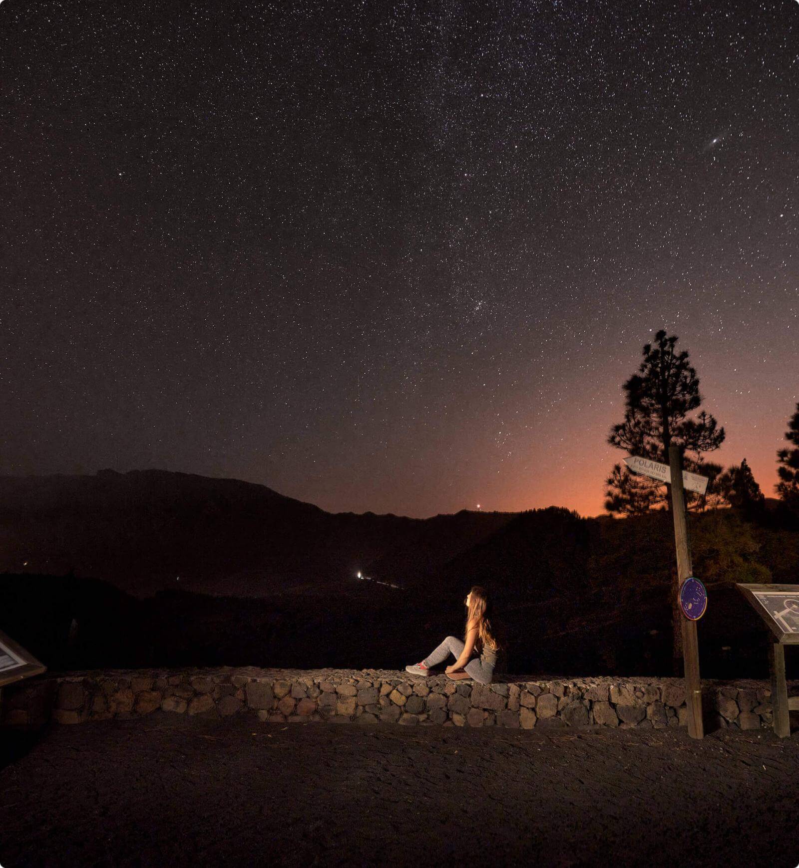Noche estrellada desde el mirador Llano del Jable, en La Palma, con siluetas de montañas y una persona observando el paisaje.
