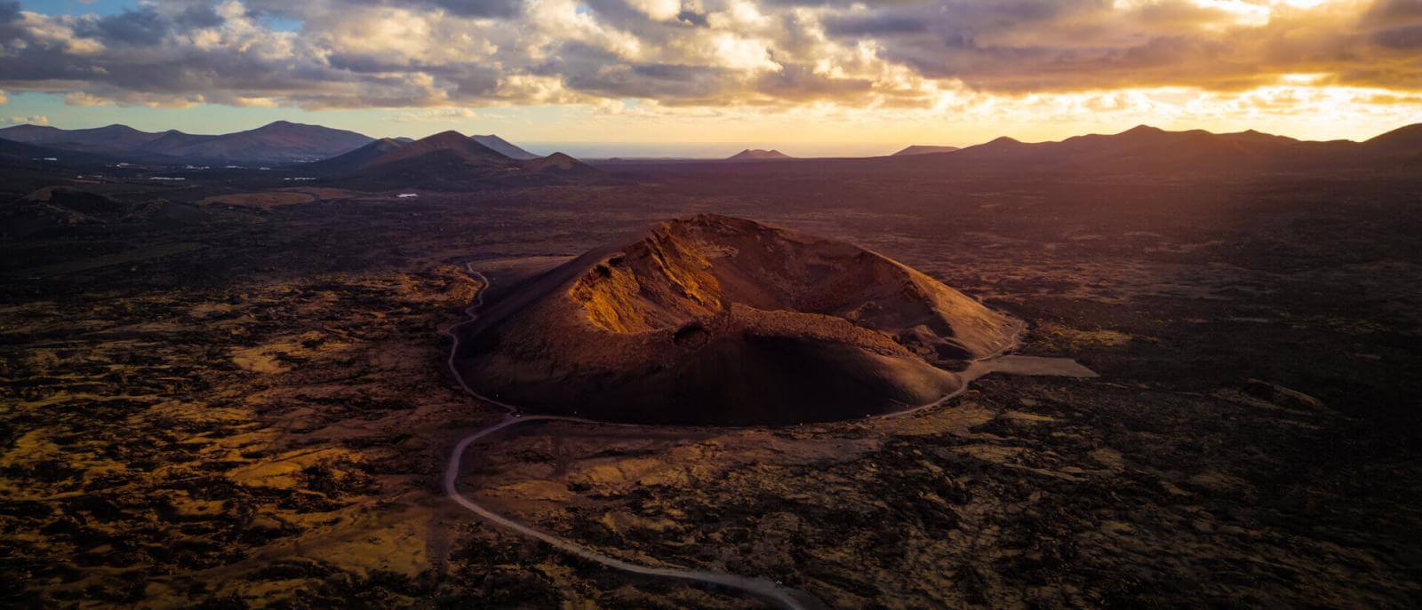 Vista aérea del Volcán del Cuervo en Lanzarote, con su cráter iluminado al atardecer y un paisaje volcánico alrededor.