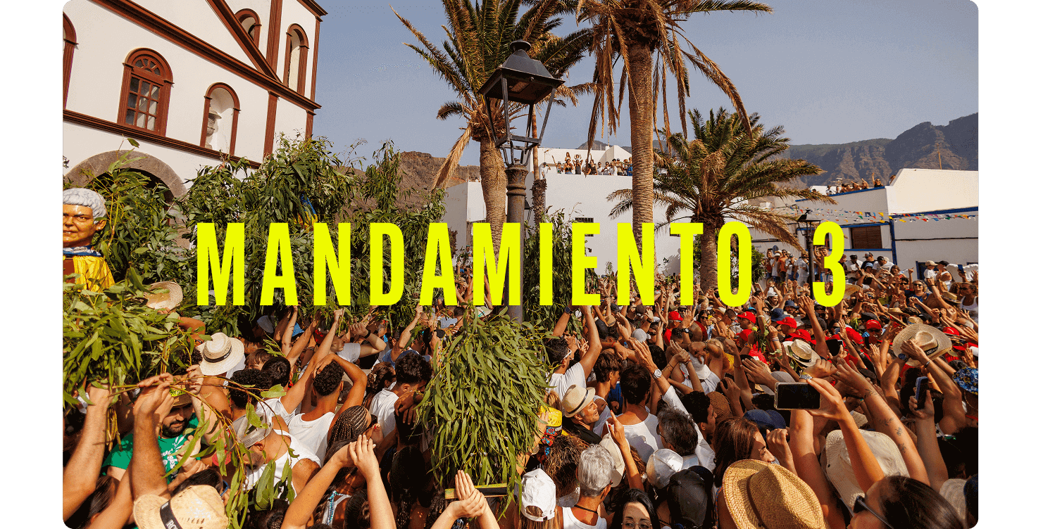 Multitud celebrando una festividad al aire libre entre palmeras y edificios tradicionales, levantando ramos verdes.