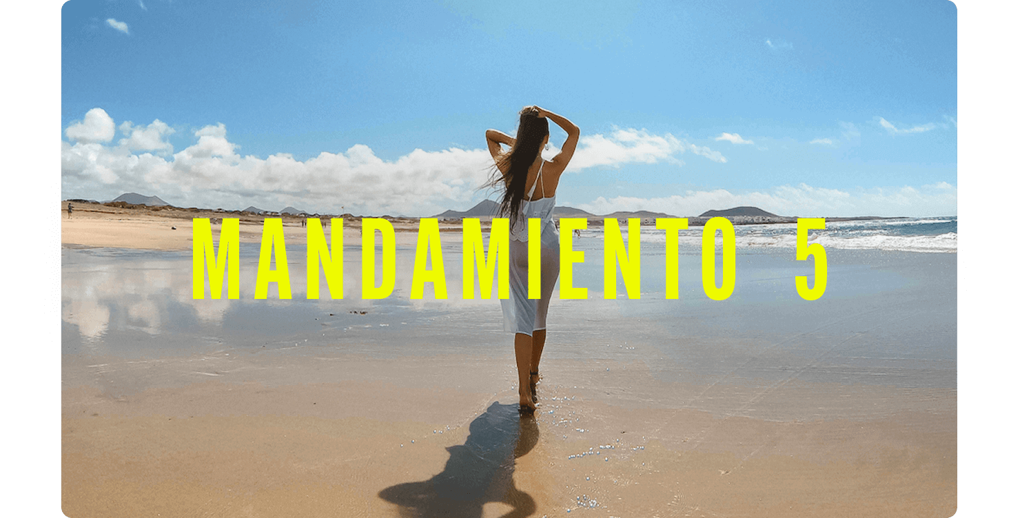 Persona de pie en la orilla de una playa amplia y tranquila, con el agua reflejando el cielo y montañas al fondo.