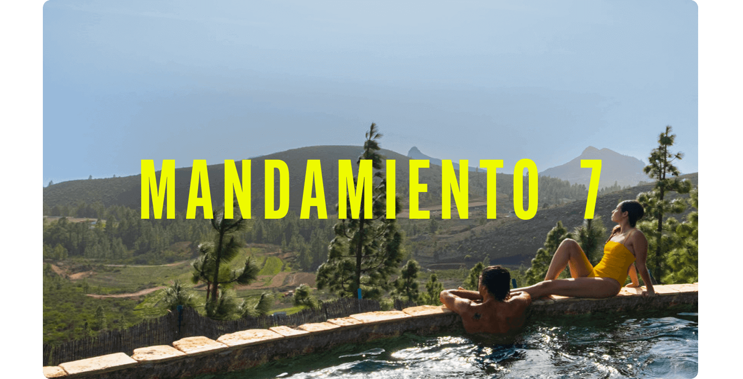 Dos personas relajándose en el borde de una piscina infinita con vistas a un paisaje montañoso cubierto de pino canario.