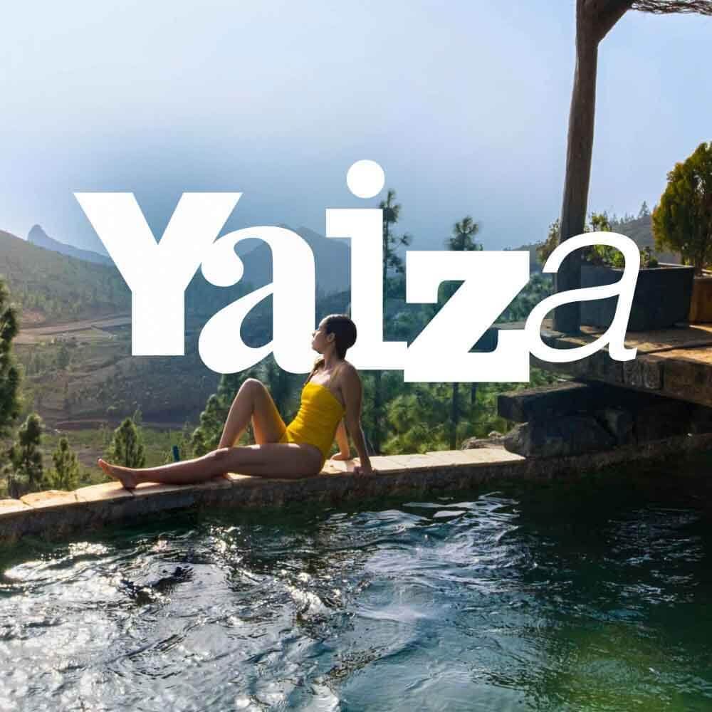 Persona junto a piscina infinita con vistas a un paisaje verde de montañas y vegetación. 