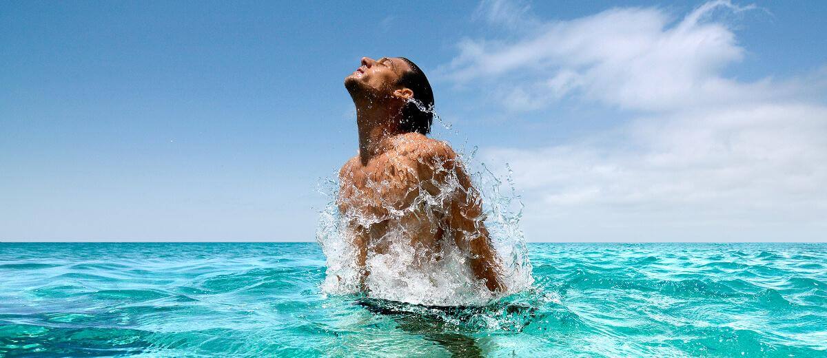 Persona emergiendo del agua en un mar cristalino, con superficie tranquila y entorno soleado.