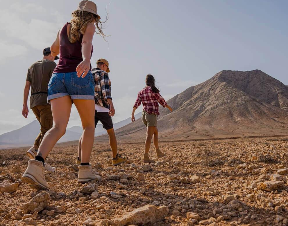 Grupo caminando por un terreno árido hacia una montaña en un entorno natural amplio.