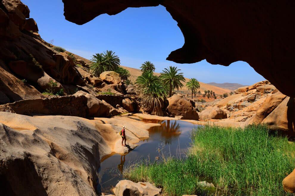 Barranco de las Peñitas en Fuerteventura, con rocas, palmeras y una pequeña poza en un paisaje árido.