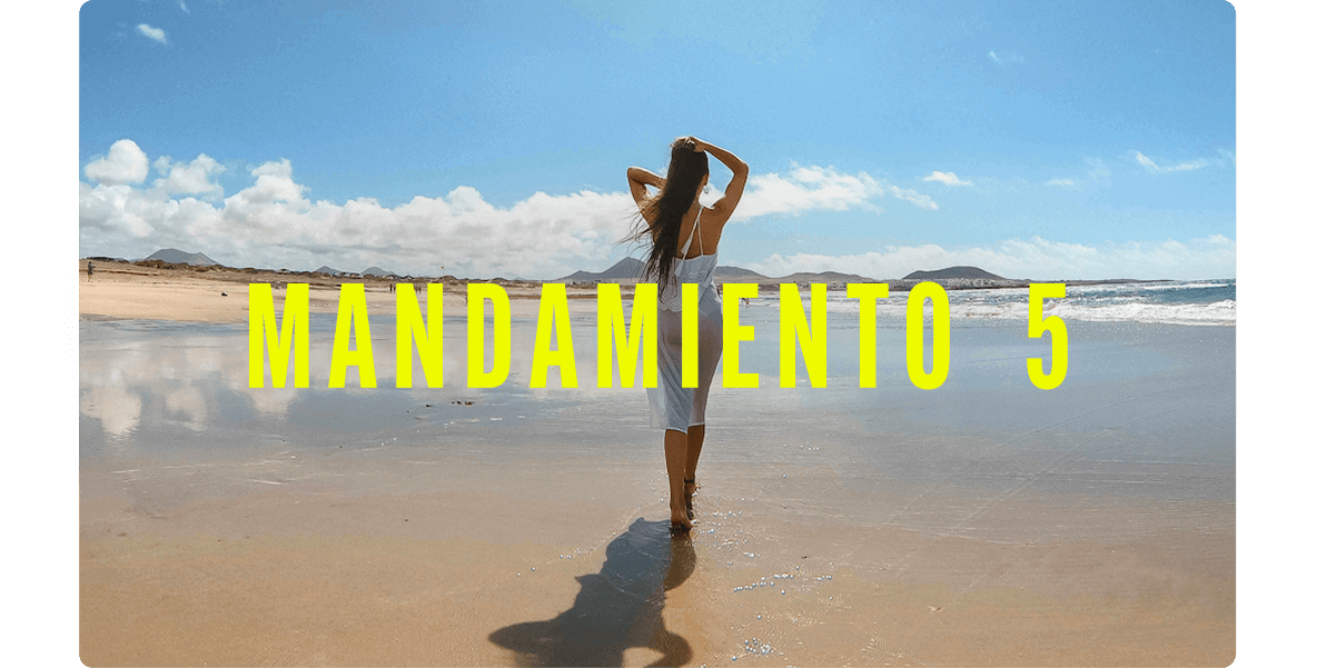 Persona de pie en la orilla de una playa amplia y tranquila, con el agua reflejando el cielo y montañas al fondo.