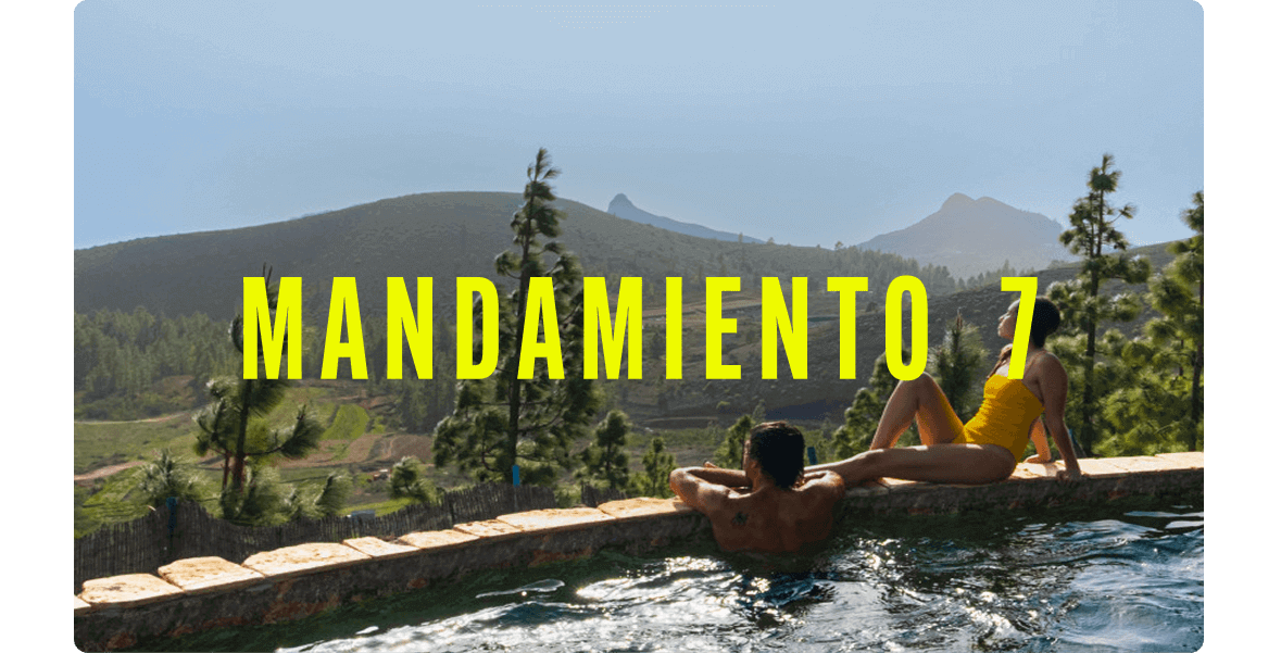 Dos personas relajándose en el borde de una piscina infinita con vistas a un paisaje montañoso cubierto de pino canario.