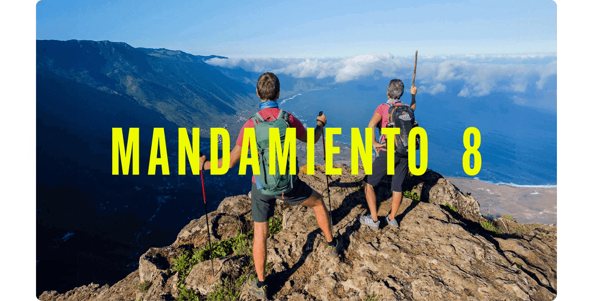 Dos personas con mochilas en lo alto de un acantilado, observando un valle verde y la costa con nubes bajas.