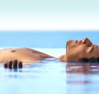 Persona flotando boca arriba en el agua en un entorno tranquilo.