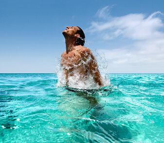 Persona emergiendo del agua en un mar cristalino, con superficie tranquila y entorno soleado.