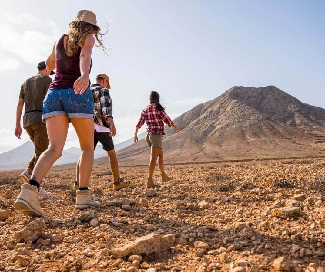 Grupo de personas caminando sobre terreno pedregoso, con paisaje volcánico al fondo.